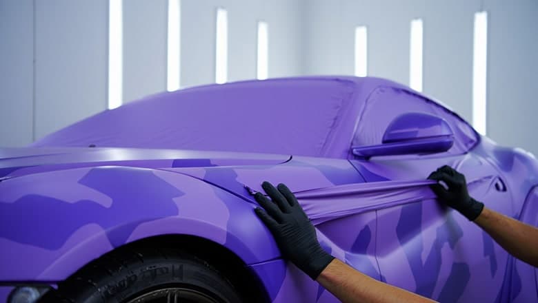 Photo de main en train d'appliquer un vinyl covering sur la carrosserie d'une voiture